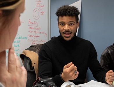 A male seated at a table discusses ideas with peers