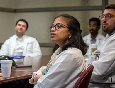 Medical students or residents sit at a table listening to a speaker